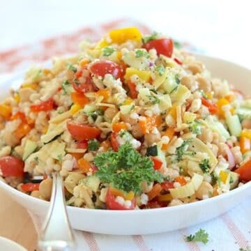 Mediterranean pearl couscous salad served in a shallow round white bowl and a silver spoon.