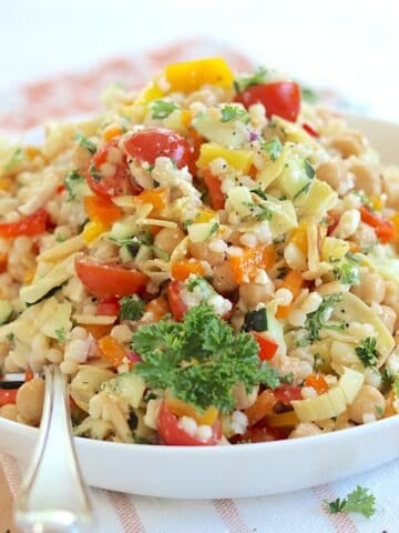 Mediterranean pearl couscous salad served in a shallow round white bowl and a silver spoon.