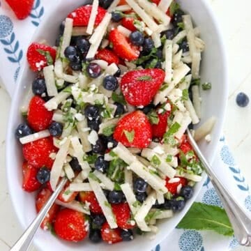 Serving a red white and blue fruit salad in a white oval bowl and two silver spoons.