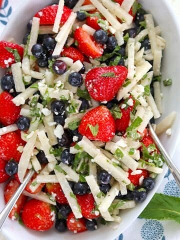 Serving a red white and blue fruit salad in a white oval bowl and two silver spoons.