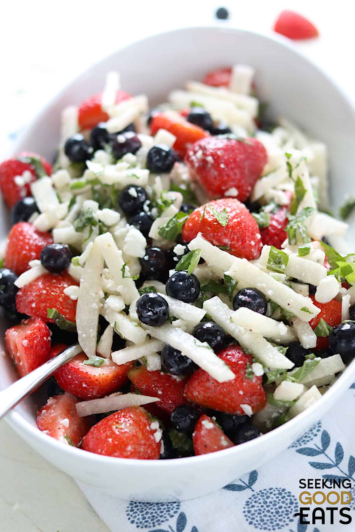 Serving the red white and blue fruit salad in an oval white serving bowl and a silver spoon.