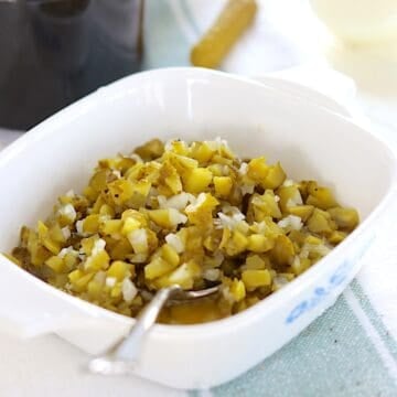 Homemade dill pickle relish in a white square serving dish and a silver spoon.