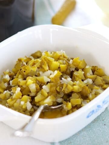 Homemade dill pickle relish in a white square serving dish and a silver spoon.