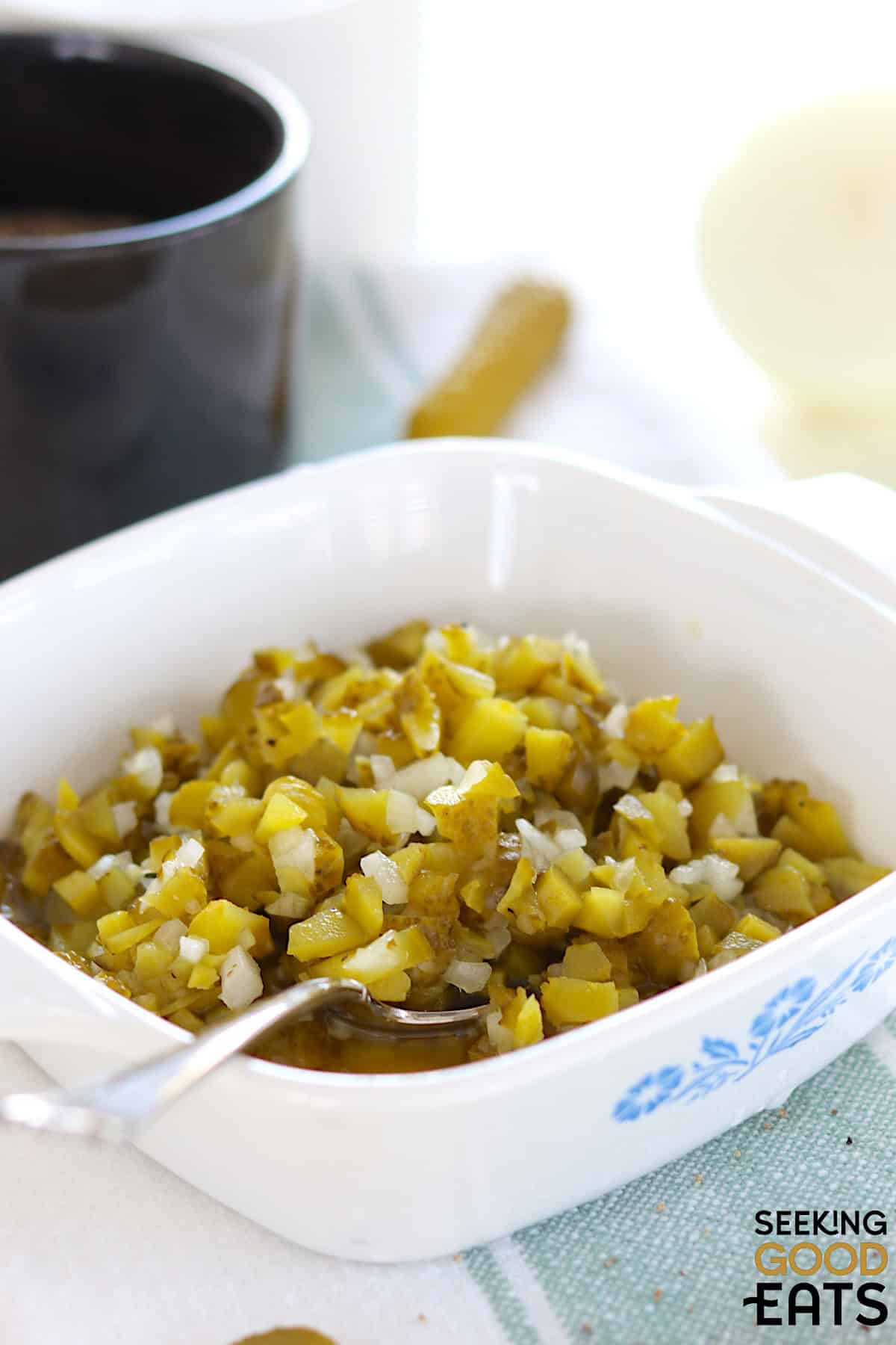 Homemade dill pickle relish served in a white square serving dish and a silver spoon.
