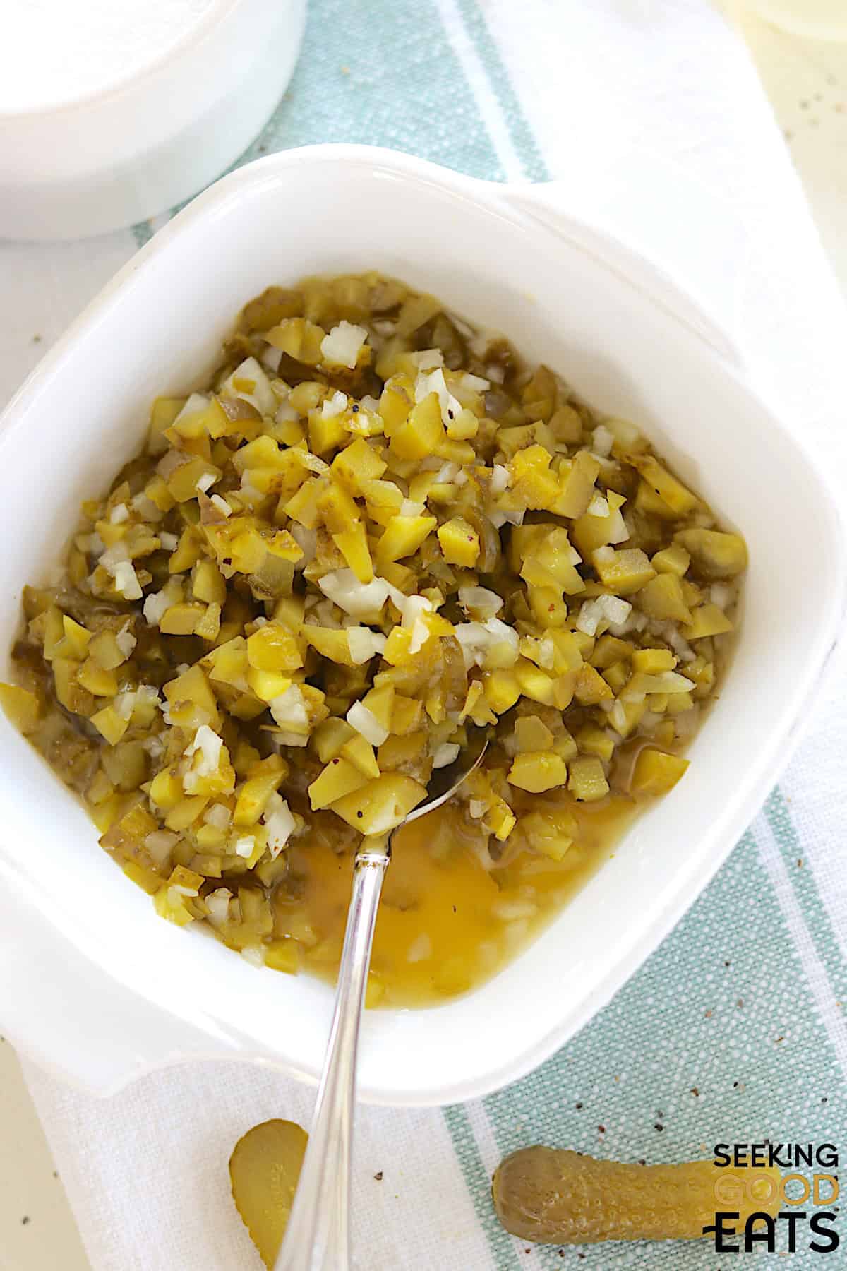 Homemade dill pickle relish served in a white square serving dish and a silver spoon.