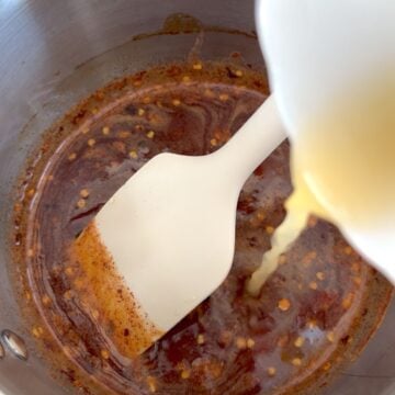 Stirring apple cider vinegar into the hot honey in a saucepan.