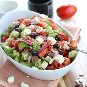 Chunky fresh Greek salad in a white oval bowl drizzled with dressing.