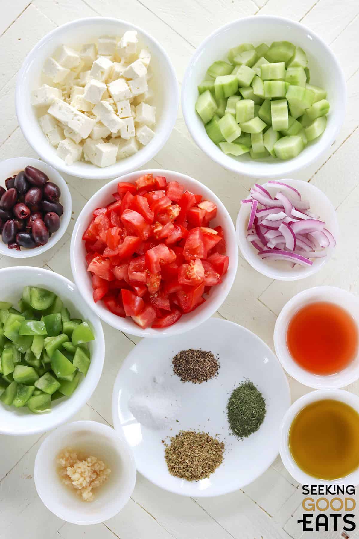 Ingredients needed for making a traditional Greek salad recipe on a white wooden board.