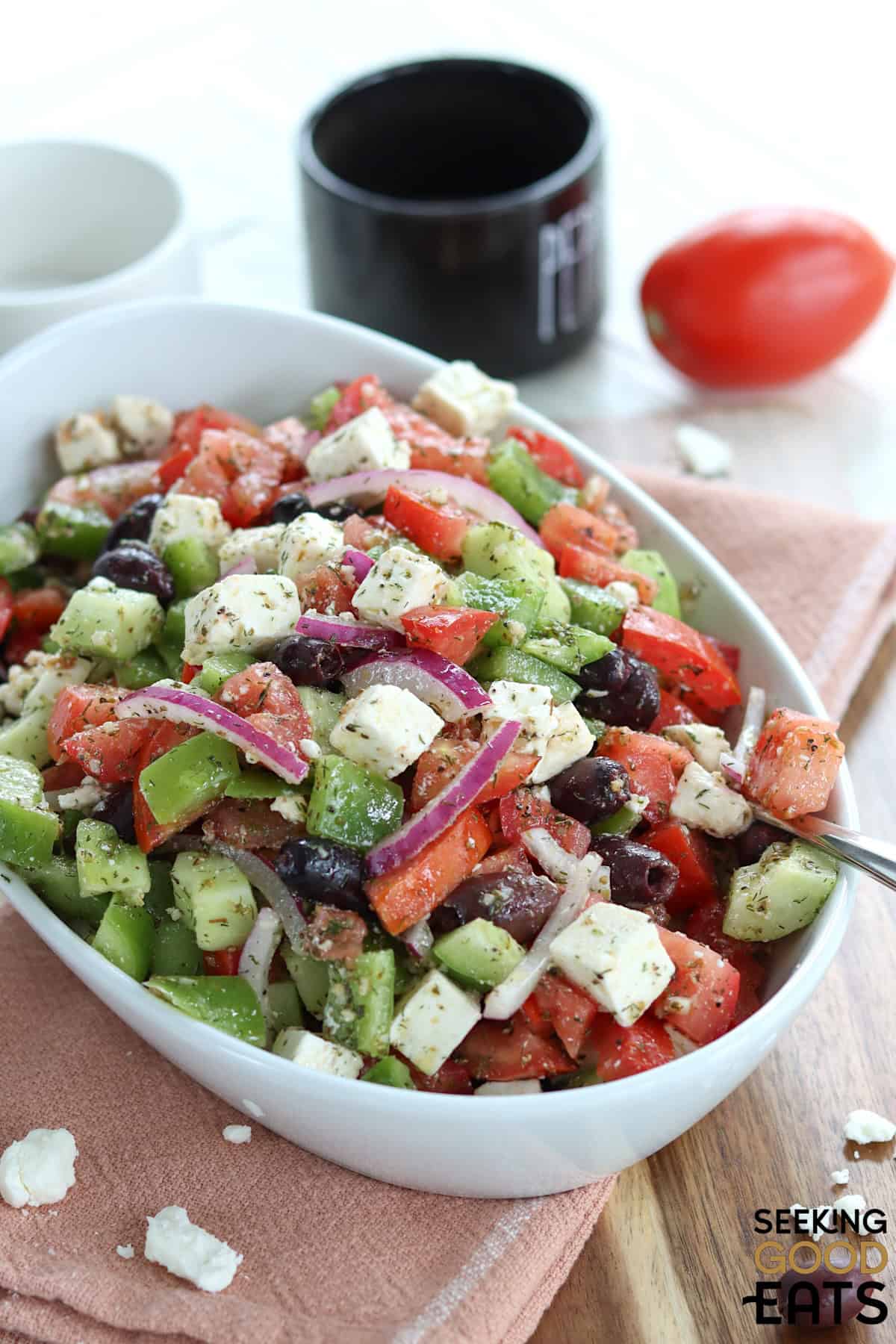 A white salad bowl of greek salad recipe on a rust colored napkin.