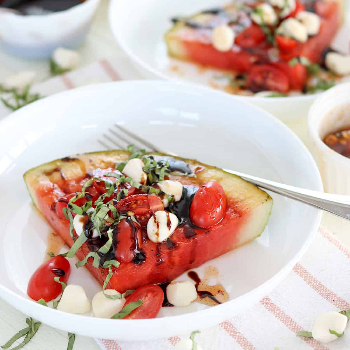 A white plate of grilled watermelon caprese wedge drizzled with hot honey.