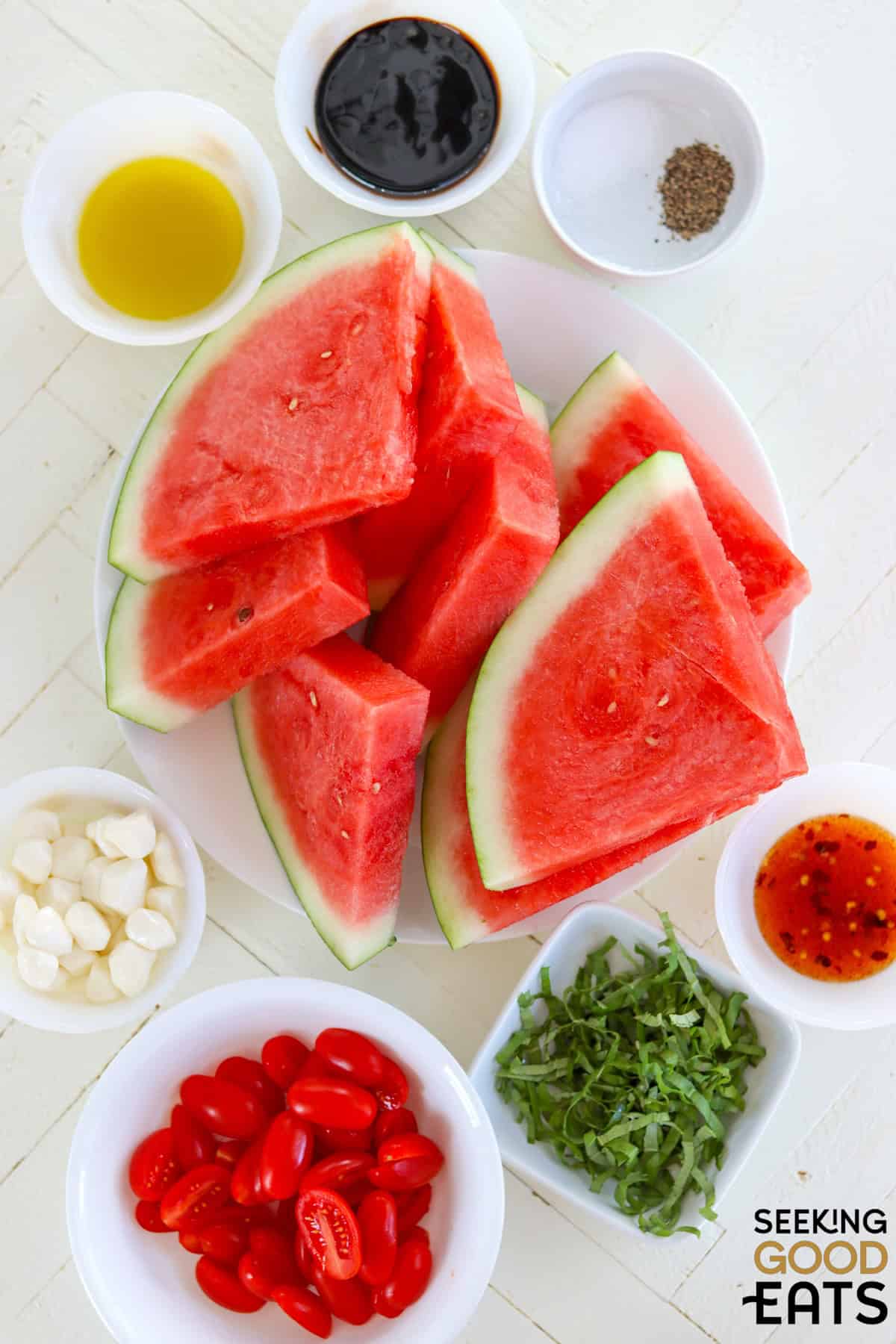Ingredients needed for making watermelon caprese salad on a white wooden board.