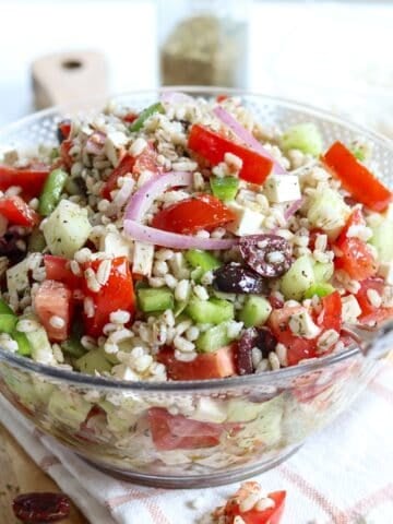 Mediterranean barley salad served in a bowl with a spoon.