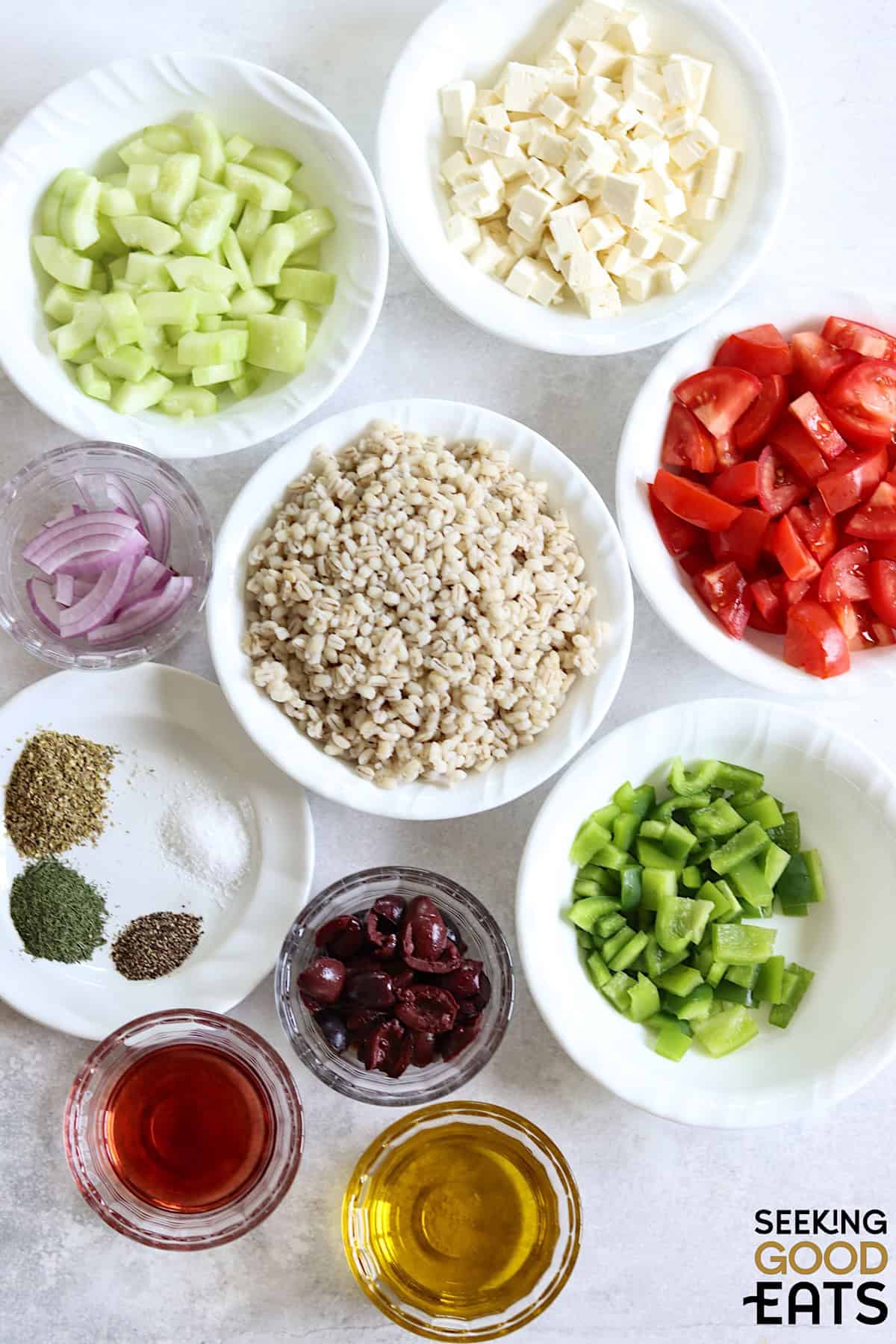 Ingredients needed for making Mediterranean barley salad on a white board.