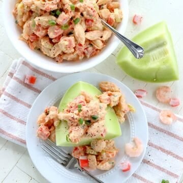 Featured image of creamy seafood pasta salad with crisp vegetables serve on a piece of melon.