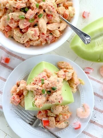 Featured image of creamy seafood pasta salad with crisp vegetables serve on a piece of melon.