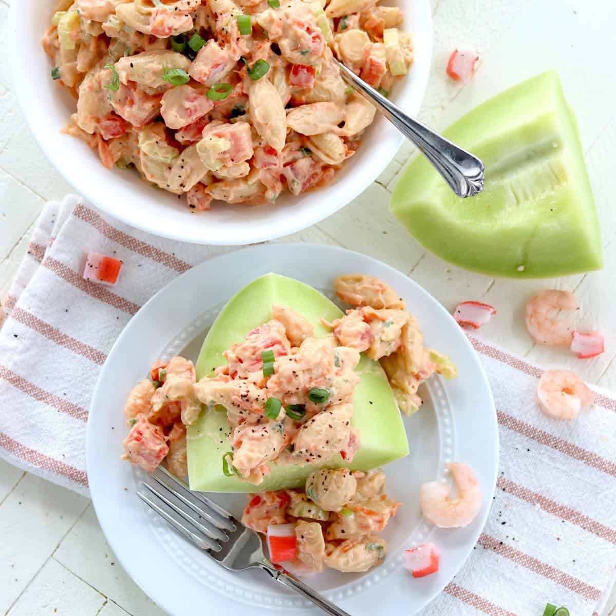 Featured image of creamy seafood pasta salad with crisp vegetables serve on a piece of melon.