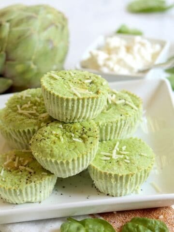 A square white plate of artichoke spinach egg bites topped with parmesan.