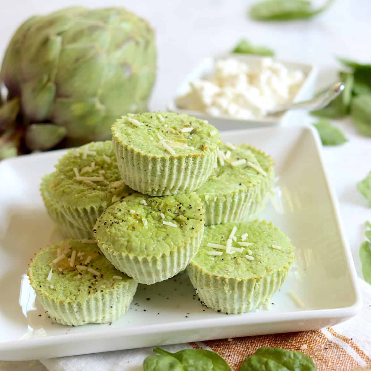 A square white plate of artichoke spinach egg bites topped with parmesan.