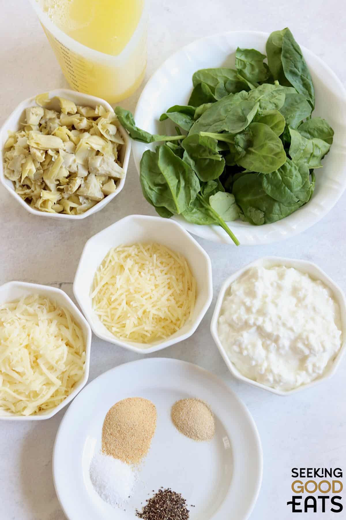 Ingredients needed for making spinach artichoke cottage cheese egg bites on a white wooden board.