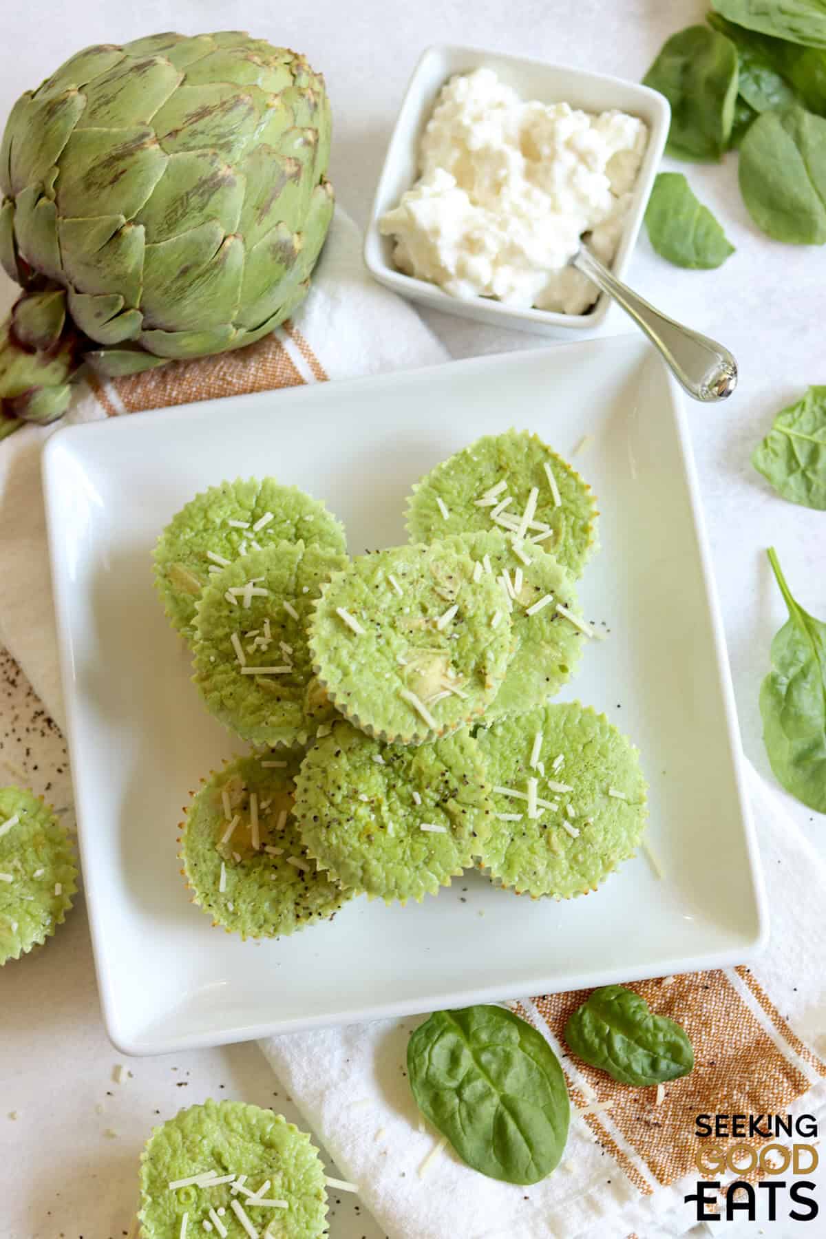 A white plate of 8 spinach artichoke egg bites with a small bowl of cottage cheese.