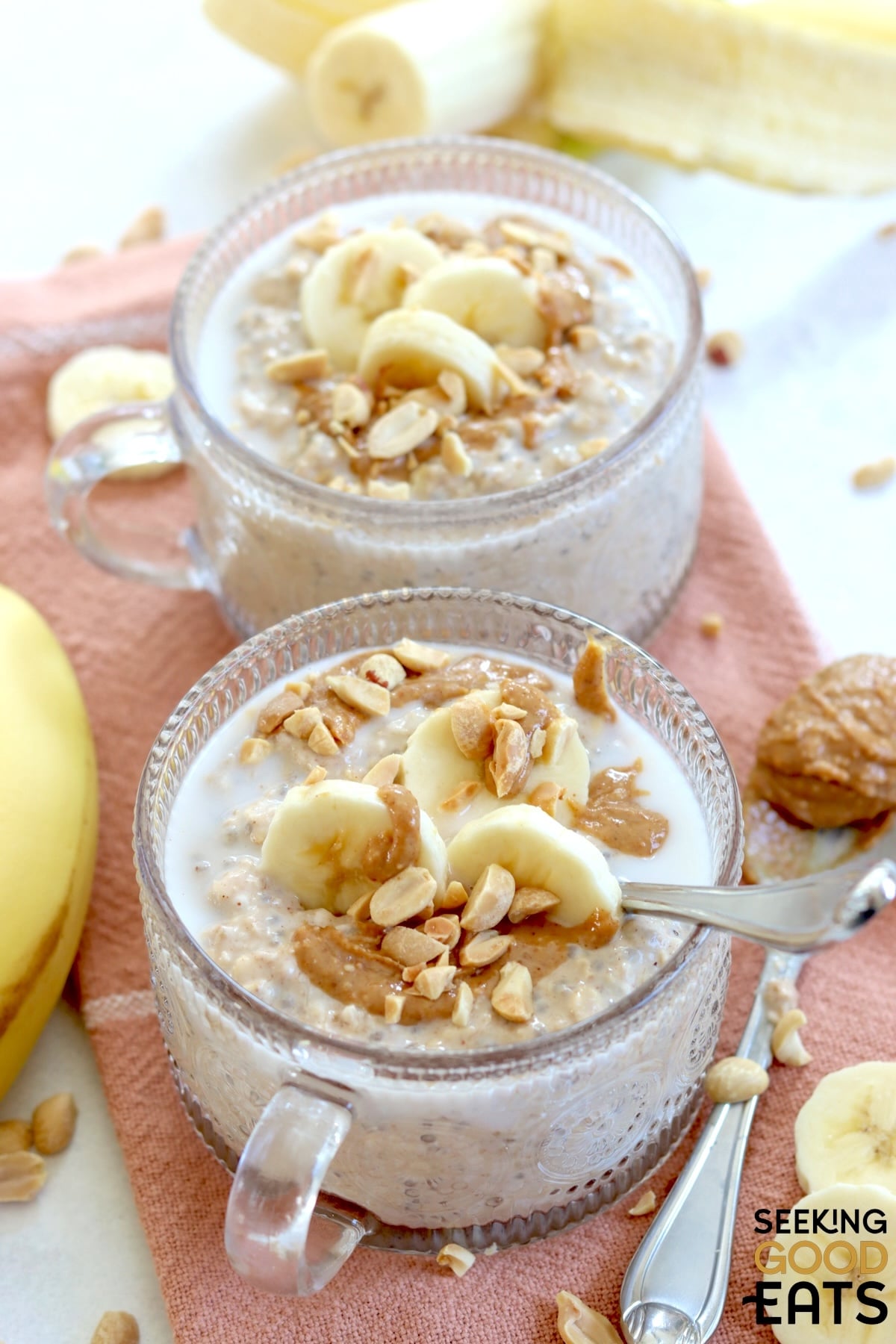 Two clear bows of overnight peanut butter banana oatmeal topped with bananas, peanuts, and peanut butter.
