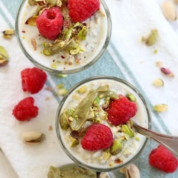 Raspberries, pistachios, and pistachio cream overnight oats in a clear glass dish with a spoon.
