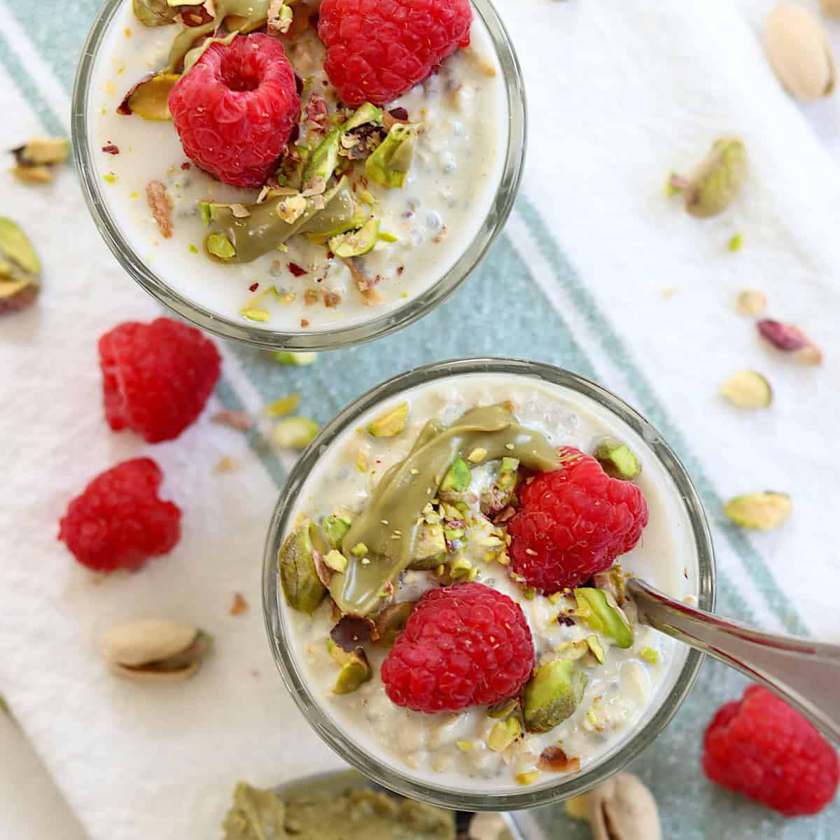 Raspberries, pistachios, and pistachio cream overnight oats in a clear glass dish with a spoon.