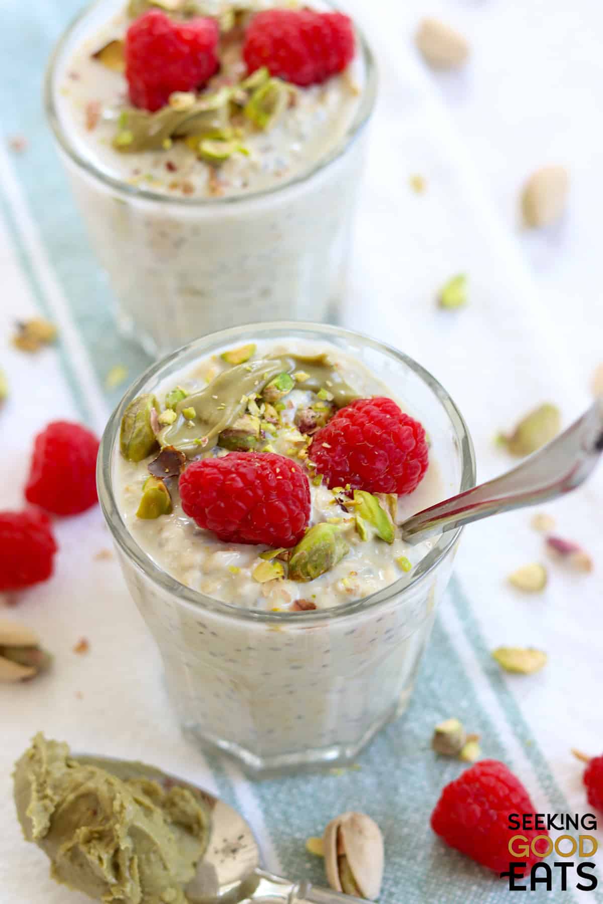 A clear dish full of pistachio and cream overnight oats topped with nuts and raspberries.