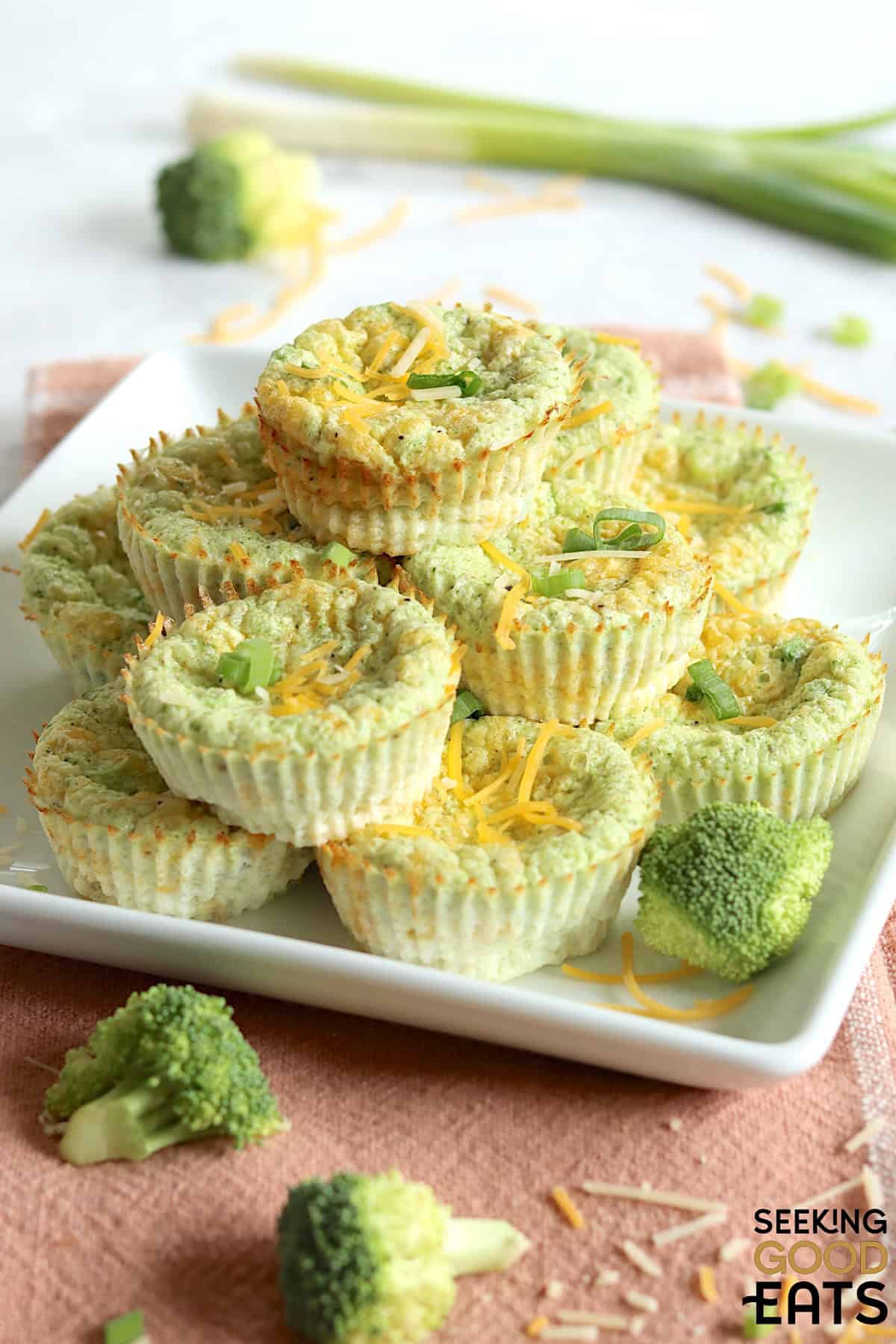 Broccoli cheese egg bites stacked up on a white plate garnished with cheese and green onions.