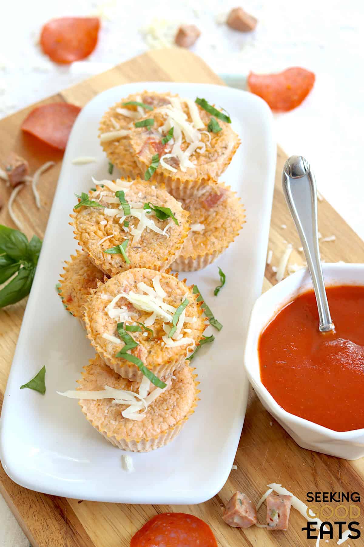 Pizza egg bites on a rectangle white plate garnished with mozzarella and basil with a side of pizza sauce.