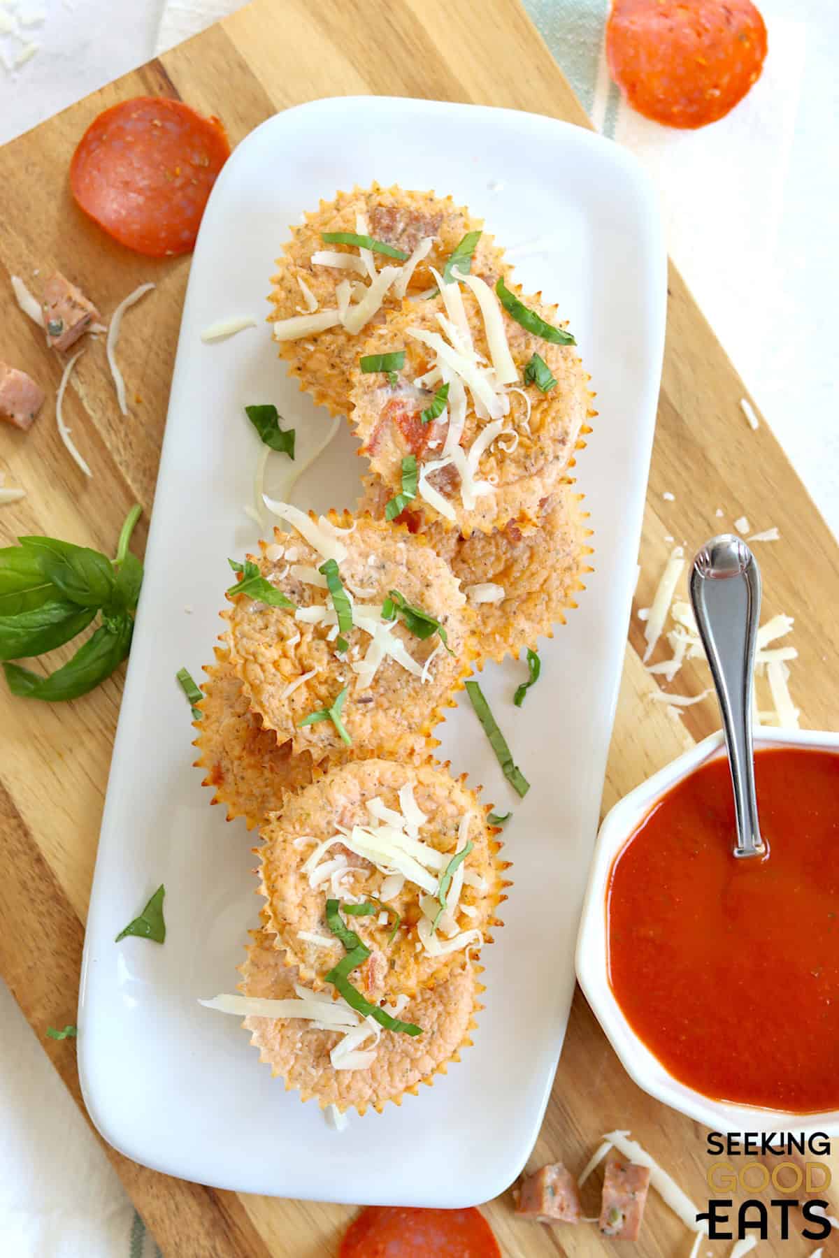 Seven cottage cheese egg bites stacked on a white plate with a side of pizza sauce with a spoon.